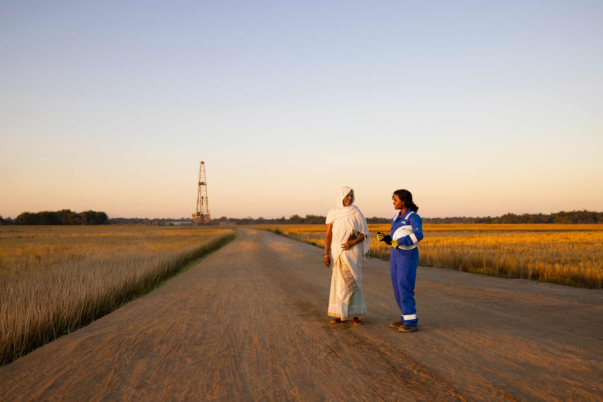 Two women along a road with a drilling rig far in the distance